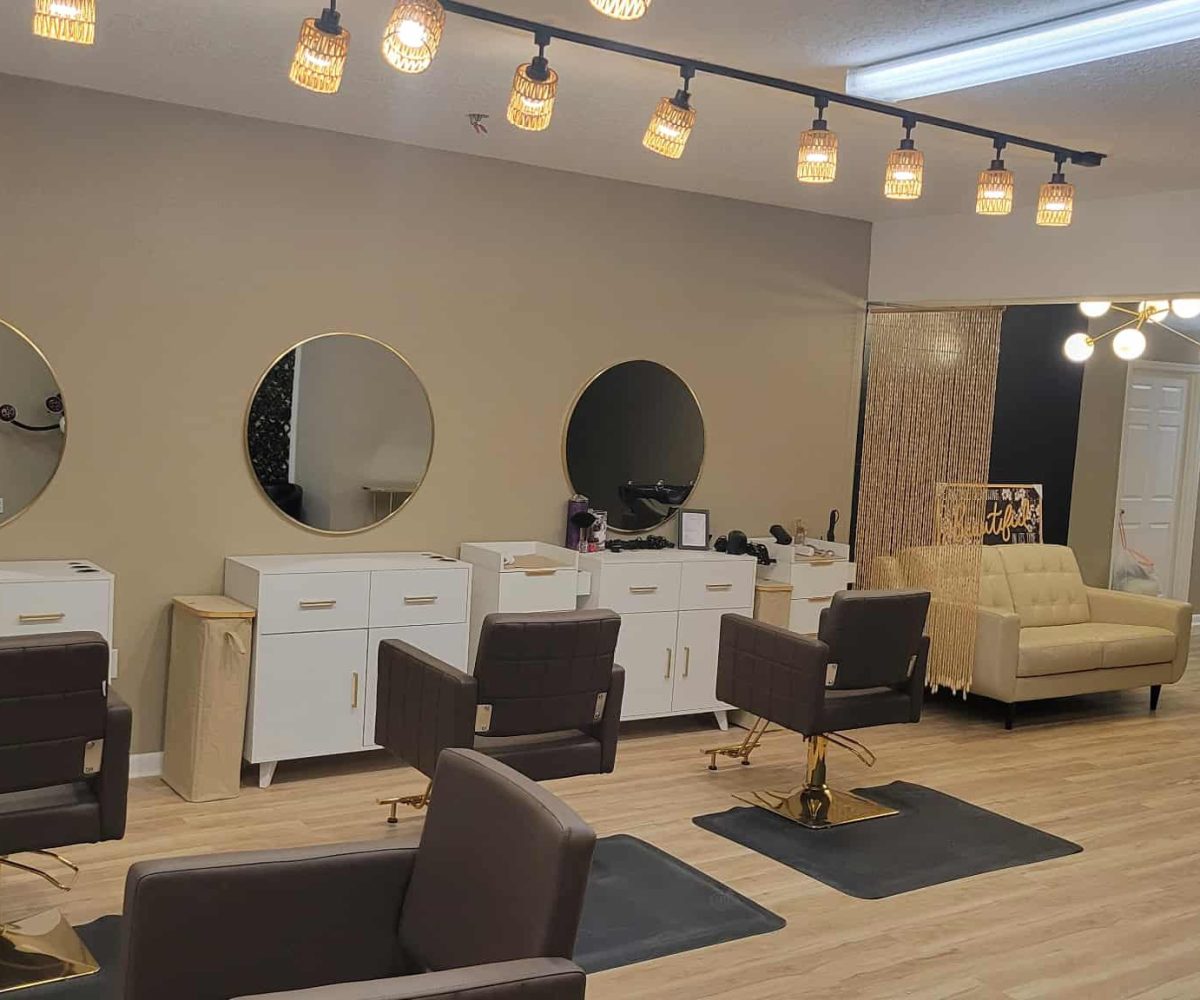 A modern Winter Haven salon interior with three ViBE styling stations, mirrors, brown chairs, white cabinets, and a beige sofa under warm lighting.